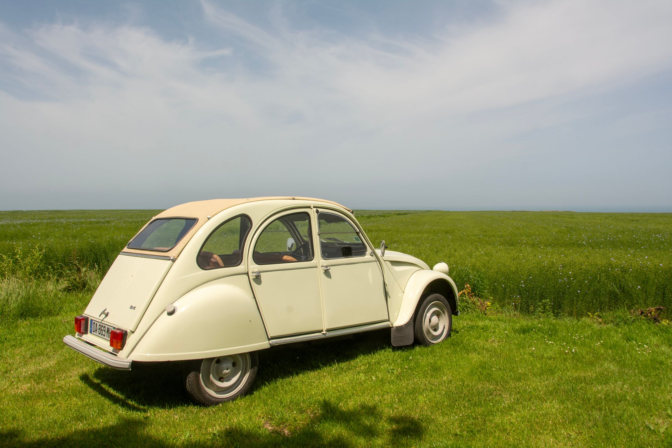 A cream-coloured classic Citroën 2CV on a country road